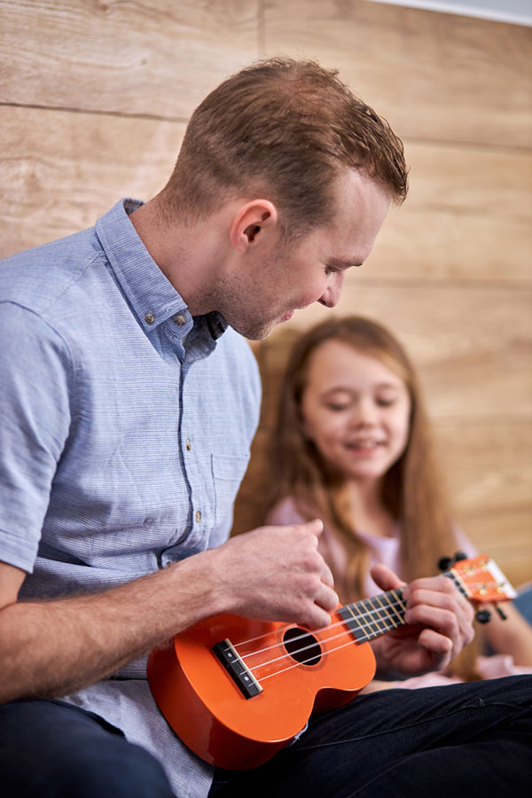 Man sitting down playing ukulele while a child watches